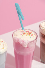 Strawberry, chocolate and vanilla milkshake with whipped cream on pink background. Place for text. Sweet drinks