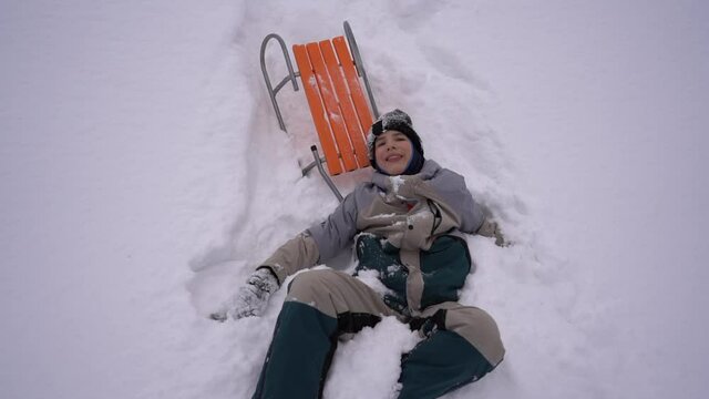 Happy schoolboy lies in the snow during winter holidays. Boy fell from a sled into the snow, fun winter activities, children's leisure