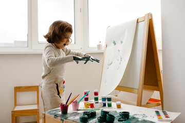 Child painting her hand with paint and paintbrush. Art therapy for children.