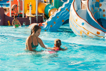 A beautiful older sister helps her little younger sister learn to swim in a pool with clear and transparent water