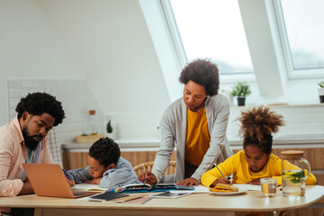 Two afro children and their parents doing homework together while sitting at the table