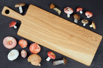 Empty wooden board decorated with wild edible various mushrooms on the black background. Top view with free copy space for text 
