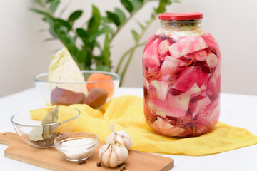 Pickled pink cabbage fermentative with beets and carrots in brine in a jar on a light background.