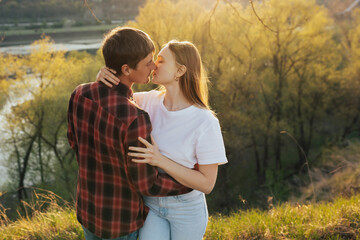 Two young people in the light of sun hugging and want to kiss at nature.