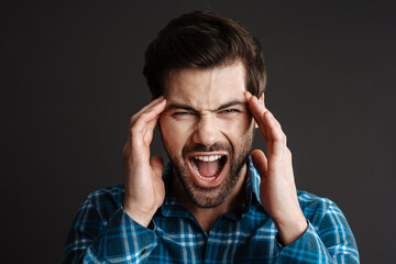 Unhappy handsome guy with headache screaming and rubbing his temples