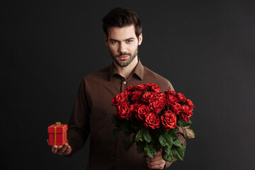 Confident handsome guy posing with gift box and bouquet of roses