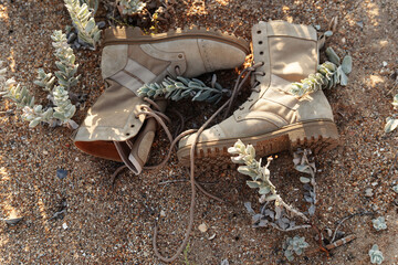 Army beige beige boots with laces lie on a background of sand and grass, the concept of outdoor activities