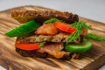 Redfish bread sandwich with cucumber, greens and tomatoes laying on a rustic board