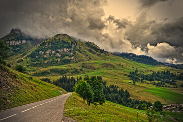 La Clusaz, France - August 9th 2017 : Mountain landscape taken near the hamlet la Clusaz, at 10 km of Albertville city. Focus on a road and wonderful green mountains in background, very cloudy.