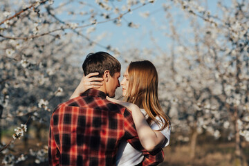 Young stylish couple is hugging near spring blossom trees. 