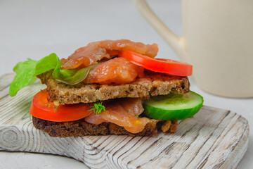 Trout bread snack with salad, vegetables and herbs laying on a white rustic board
