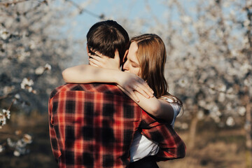 Beautiful couple in love is hugging  in spring nature. Loving man and woman on a walk in a spring blooming park.