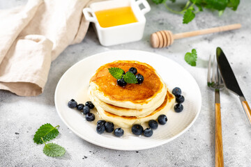 Pancakes in a white plate on the light gray kitchen table. Homemade delicious pancakes with honey and blueberries
