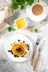 Pancakes in a white plate on the light gray kitchen table. Homemade delicious pancakes with honey and blueberries. Delicious sweet and hearty breakfast
