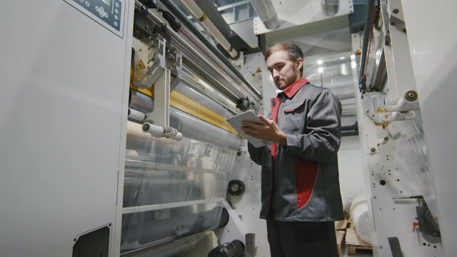 Medium slow-motion footage of caucasian foreman with digital laptop checking production of polyethylene film at factory