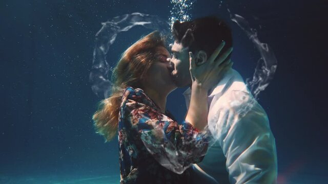 Cinematic shot of young carefree romantic loving couple is kissing with passion in blu underwater with water splash in heart shape. Concept of love, relationship, freedom, sensuality, fantasy.
