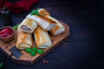Pancakes stuffed with meat on wooden board with sauce and fresh herbs, selective focus