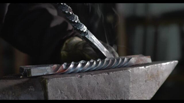 Unrecognizable forger putting metal details on anvil in workshop