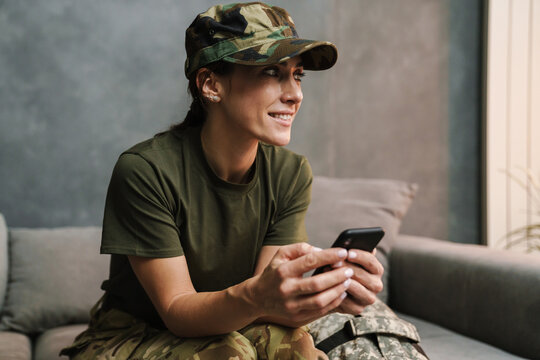 Smiling beautiful soldier woman using mobile phone while sitting on sofa