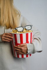 Popcorn paper bucket and 3D glasses in the hands of a young girl preparing to watch a movie. Showtime. Eating delicious unhealthy sweet snacks. Going to cinema for a new film. Rest and entertainment