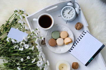 white wooden tray with black tea, coffee, plate with macaroon cakes, flowers, candles, notebook with blank sheets for text, concept lifestyle, joys of life, top view
