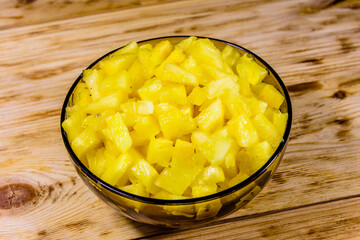 Glass bowl with chopped pineapple on wooden table