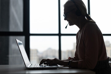 Side view a silhouette of female call center employee using a headset and laptop for online...