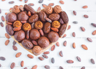Heart shaped box with chocolates and coco beans around on a white wooden background. Flat lay. Valentine's day, love,