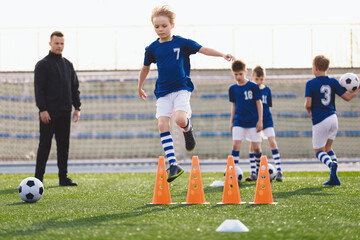 Kids on sports soccer training. Boys running balls and jumping over cones. Agility exercises for youths in football team. Coach of football team coaching players. Kids making training drills program
