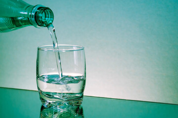 A glass on the table is filled with water from a bottle. Sparkling water . Plastic bottle. Gas bubbles in water. Copy space.