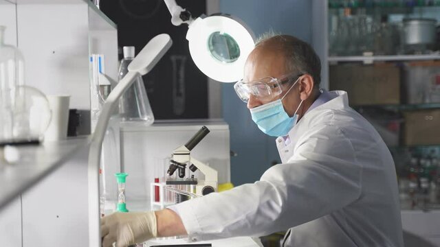 Scientist, researcher conducts research or experiment by using microscope. Senior professor chemist at work place in laboratory, biology microbiology concept.
