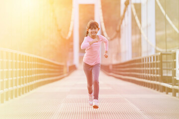 Happy girl jogging in the evening sunlight on the bridge over the river, fitness concept and color tone background in yellow.