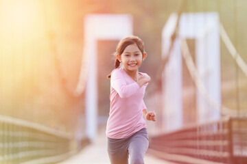 Happy girl jogging in the evening sunlight on the bridge over the river, fitness concept and color tone background in yellow.