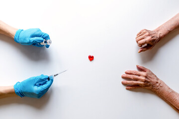 Medical syringe and ampoule with medicine in the hands of a doctor in medical gloves on a white background, the outstretched hands of an elderly woman.