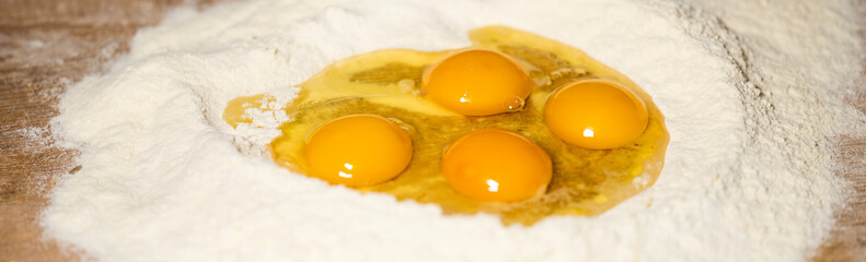 (Selective focus) Close-up view of a heap of flour with some fresh eggs inside. Flat lay, Ingredients for a homemade dough such as pasta, bakery, cakes etc.