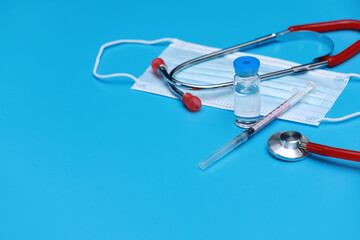 Medical bottle, vial, syringe, stethoscope and face mask on blue background with copy space. Vaccination session and immunity improvement.