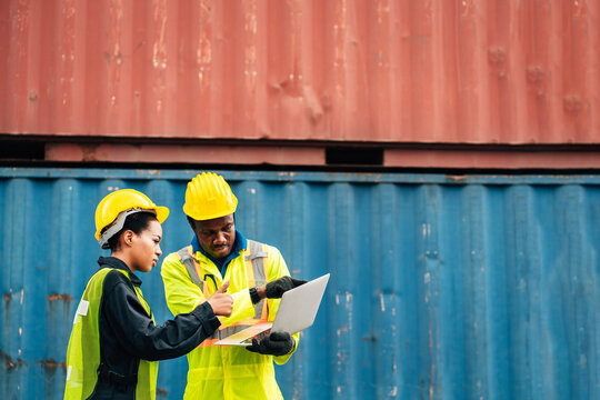 workers teamwork man and woman in safety jumpsuit uniform with yellow hardhat and use laptop check container at cargo shipping warehouse. transportation import,export logistic industrial service