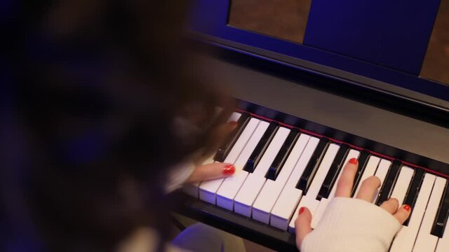 Female young hands playing piano in red manicure and accessories. Unrecognizable girl playing piano keywords close-up. Classical music pattern