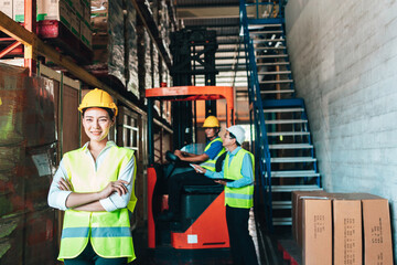 Portrait of asian woman. warehouse Smiling worker standing with arms crossed in large warehouse with goods. in background driver at Warehouse forklift loader works with goods.