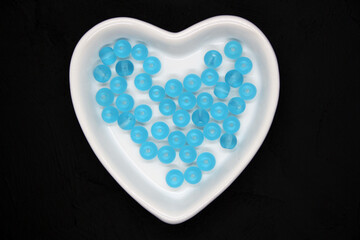 Blue beads in a heart-shaped bowl on a black background.