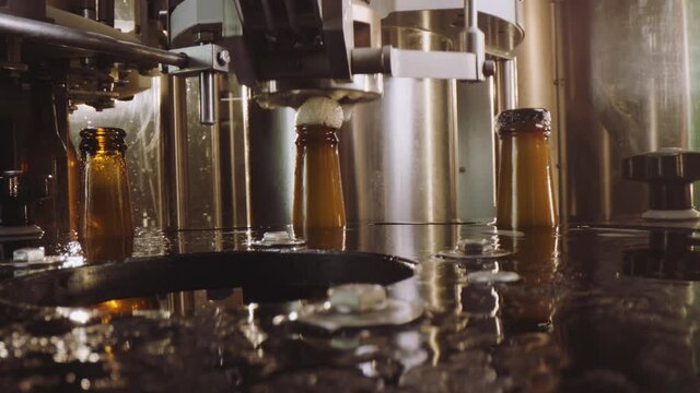 Close-up video of a modern machine capping beer bottles in a factory. Beer foam overflowing the bottles. Factory, brewery concept.