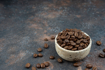 Roasted coffee beans in a ceramic bowl - selective focus. Scattered coffee beans on a dark background.Flat lay with copy space. Tip view with place for text. High quality photo. Close up. Macro.