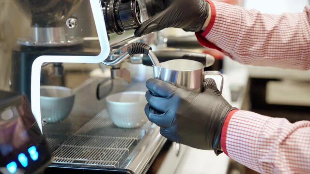 Barista steaming milk in a pitcher with professional coffee machine close up