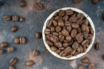 Roasted coffee beans in a ceramic bowl. selective focus. Scattered coffee beans on a dark background.Flat lay with copy space. Tip view with place for text. High quality photo. Close up. Macro.