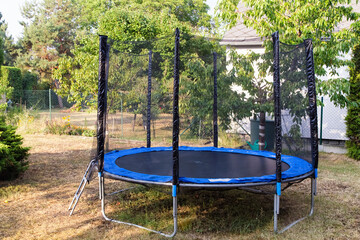 Trampoline with safety net on the lawn in a backyard. Front view of trampoline in a garden....