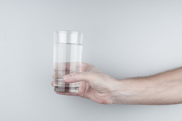 Hand holding glass of pure water on gray background