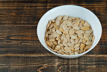 Pumpkin seeds in a white bowl on an old shabby board. Nuts on a brown wooden table.