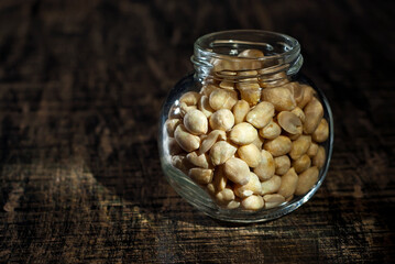 Peanuts in a glass transparent jar. Nuts on an old shabby board. Jar on a brown wooden table close...