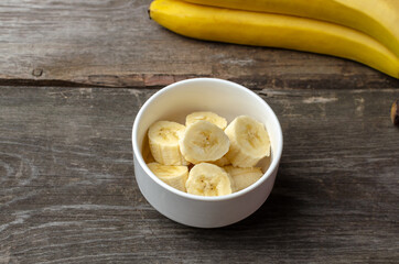 Slices of bananas in a white plate on a rustic wooden background preparing for cooking.
