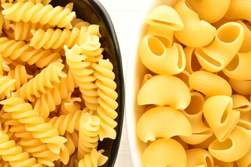 Bright yellow Pipe and Fusilli pasta in white and black ceramic dishes on a wooden table, close-up,...
